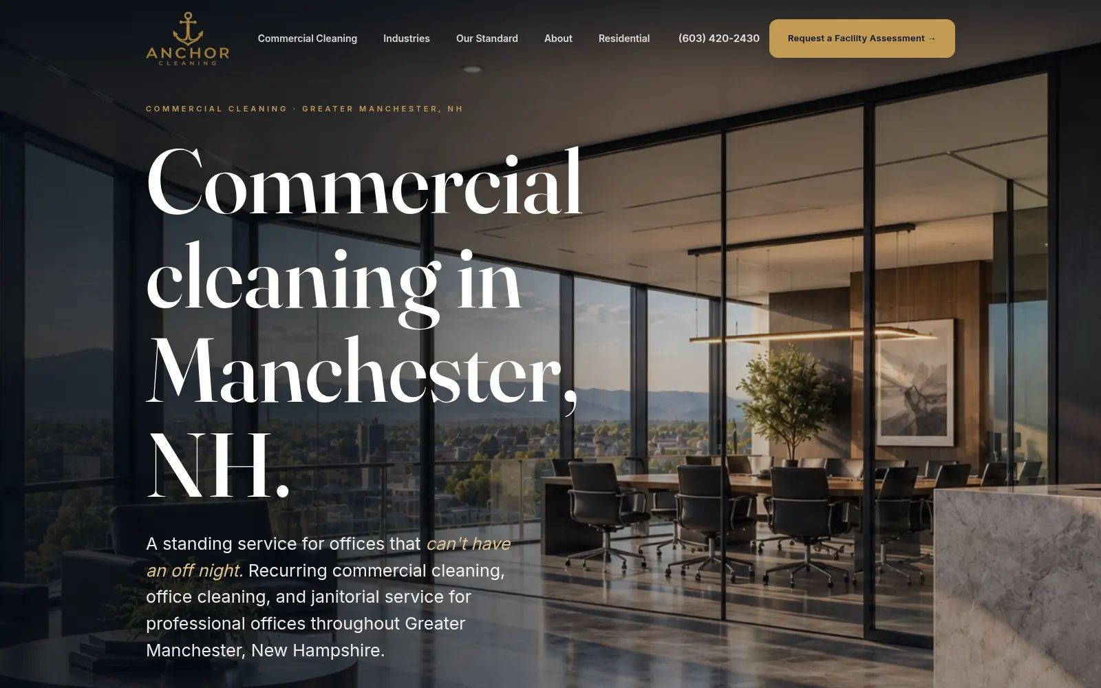 The Anchor Cleaning home page. A photographic interior of a glass-walled office fills the frame. Over it, in a large brass-and-white serif, the headline reads Commercial cleaning in Manchester, NH. A single brass button in the header reads Request a Facility Assessment.
